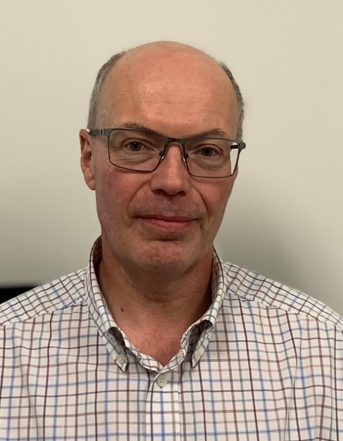 A middle-aged man with glasses and a checkered shirt, smiling and facing the camera.