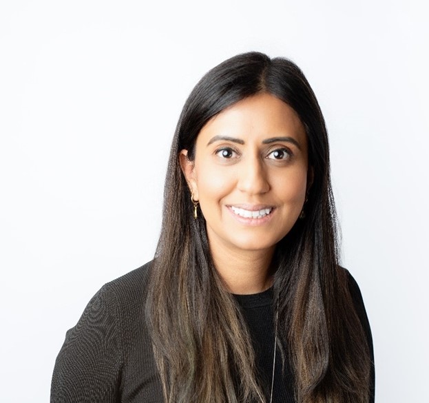 Professional headshot of a woman with long black hair, wearing a black sweater, and smiling confidently against a plain white background.