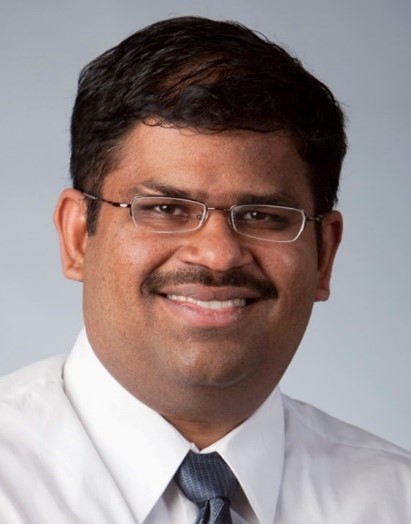 Professional headshot of a man with glasses, smiling and wearing a white shirt with a tie.